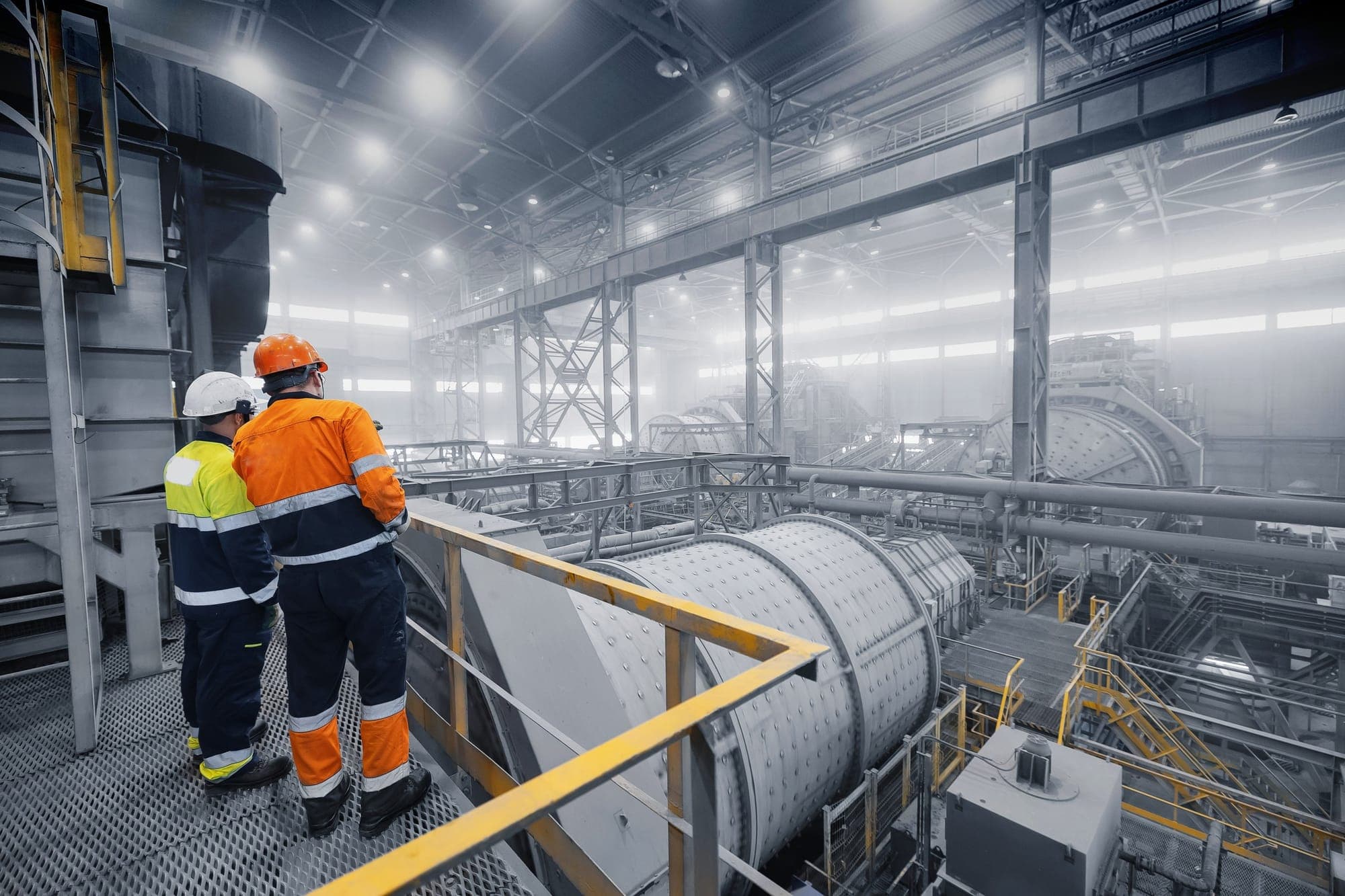 Two operators on a platform looking over the grinding mills of a concentrator